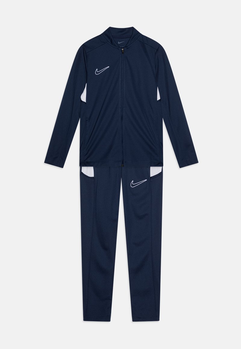 Ensemble de sport bleu marine en tissu respirant, avec des accents blancs, veste zippée et pantalon à taille élastique muni de poches.