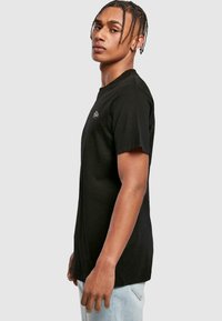 Black cotton t-shirt featuring a crew neck and short sleeves. Subtle logo on the chest, straight cut, slightly loose fit.