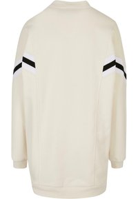 Světle béžová mikina s kulatým výstřihem, dlouhými rukávy a černobílými pruhy na ramenních švech. Měkká, strukturovaná tkanina.