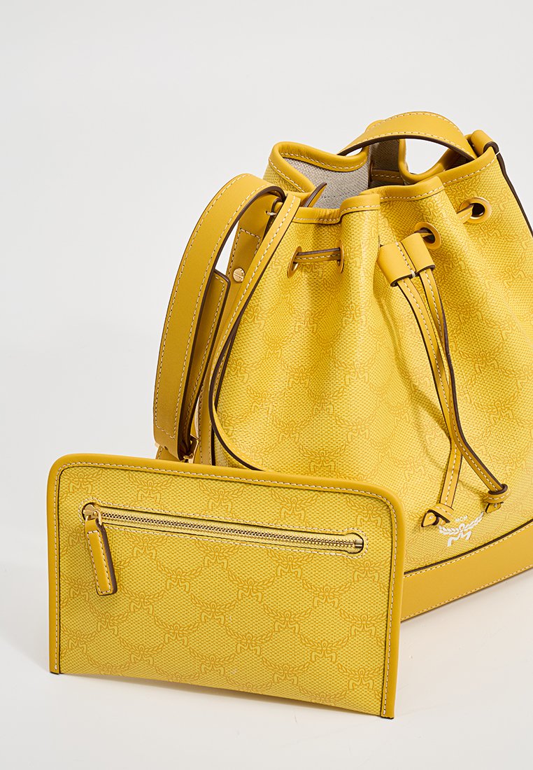 Gelbe Bucket Bag mit gemustertem Textil, Zugbandverschluss und einer flachen Geldbörse mit einem Reißverschlussfach, beide in passenden Farben.