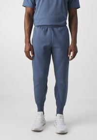 Niebieskie dresy z elastycznym paskiem w talii, zwężanymi nogawkami i bocznymi kieszeniami. Wykonane z miękkiej tkaniny, w połączeniu z białymi butami sportowymi.