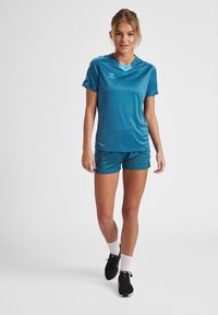 Turkis atletisk antrekk bestående av en kortermet skjorte og matchende shorts. Glatt stoff med minimal merkevare og en avslappet passform.