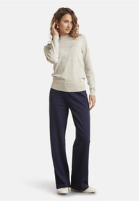 Light gray knit sweater, round neckline, ribbed cuffs, paired with dark navy wide-leg pants. Model wearing white sneakers.