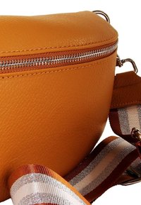 Oranje leren crossbodytas met ritssluiting, voorzien van een gestreepte stoffen band in bruin, crème en oranje. Gladde textuur.