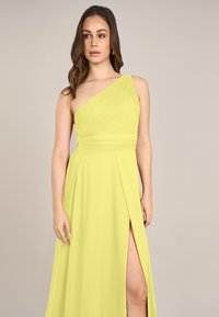 Gelbes asymmetrisches Kleid mit fließendem Stoff, strukturierten Falten, einem hohen Schlitz und einer taillierten Passform, das eine schlanke und elegante Silhouette bietet.