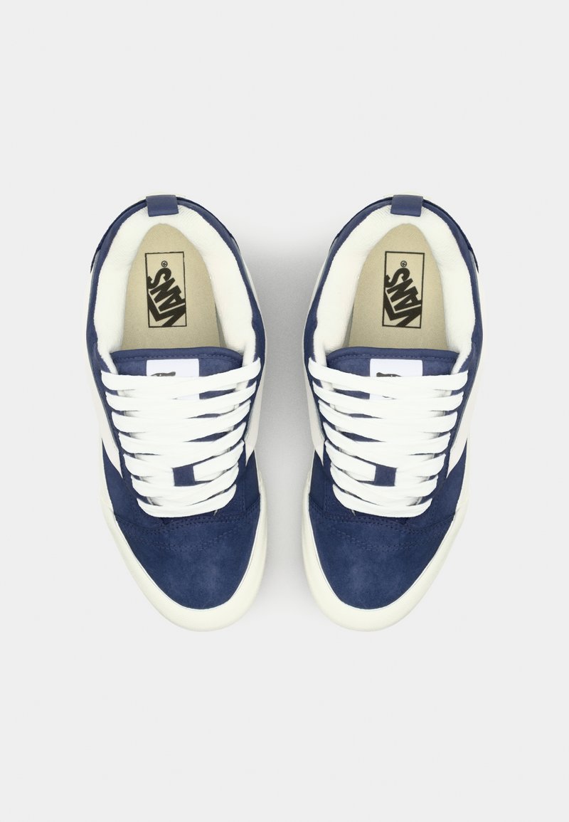 Marineblaue Wildleder-Sneaker mit weißen Schnürsenkeln und seitlichen Streifen, ausgestattet mit einem gepolsterten Innenraum und Gummisohlen. Logo auf der Zunge.