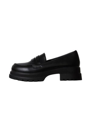 Mocassin en cuir noir avec semelle crantée épaisse et petit talon bloc, vue de côté sur fond blanc.