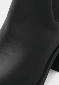 Primo piano di un elegante stivaletto in pelle nera liscia con cuciture visibili e pannello laterale elasticizzato.