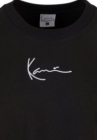 Black sweatshirt featuring a round neck, ribbed cuffs, and a white embroidered signature on the chest. Soft, cotton-like texture.