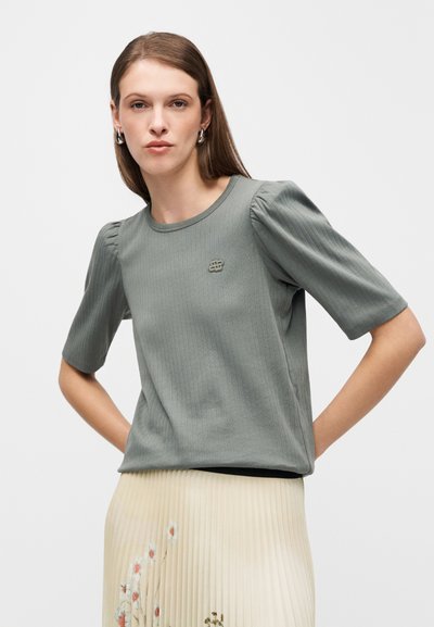 Ανοιχτό πράσινο ribbed μπλουζάκι με κοντά φουσκωτά μανίκια και στρογγυλή λαιμόκοψη. Διαθέτει μικρό λογότυπο στο στήθος και λεία υφή υφάσματος.