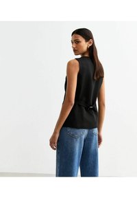 Svart ärmlös topp med en strukturerad design och en knytning på ryggen, kombinerad med ljusblå vida jeans. Slät tygtextur.