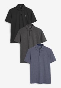 Tres camisetas polo: negra, gris oscuro y azul marino con rayas blancas. Cada una tiene un cuello tipo polo y mangas cortas, y presenta un pequeño logo en el pecho.