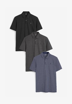 Drie poloshirts: zwart, donkergrijs en marineblauw met witte strepen. Elk heeft een kraag en korte mouwen, en een klein logo op de borst.
