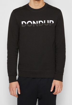 Mann trägt einen schwarzen Pullover mit weißem und schwarzem, mehrschichtigem "DONDUP"-Schriftzug auf der Brust, kombiniert mit einer schwarzen Hose.