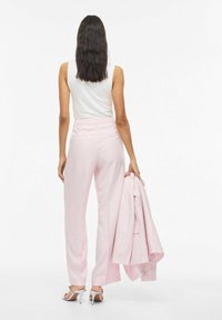 Pantalon rose sur mesure à taille haute et coupe droite; associé à un haut blanc sans manches et un blazer rose assorti porté sur le bras.