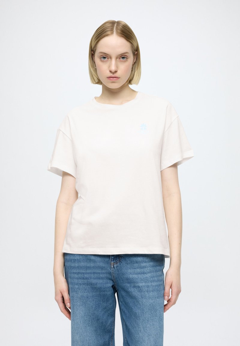 Tricou din bumbac bej deschis, cu mâneci scurte și gât rotund. Are un logo mic albastru pe partea stângă a pieptului. Asortat cu pantaloni scurți din denim albastru.