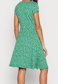 Zielona sukienka z krótkim rękawem, cechująca się dopasowaną górą i rozkloszowaną spódnicą, ozdobiona białymi kropkami oraz miękką, gładką teksturą materiału.