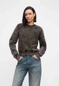 Μαύρο φθαρμένο φούτερ με ριμπ μανσέτες, στρογγυλή λαιμόκοψη και διακοσμητικές ραφές στα μανίκια. Συνδυάζεται με ανοιχτό μπλε τζιν παντελόνι.