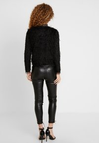 Svart fluffig tröja med långa ärmar, parat med svarta, tighta läderbyxor. Outfiten har en elegant, blank yta och minimal detaljering.