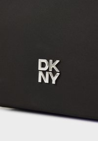 Sort tekstureret stoftaske med et fremtrædende sølv DKNY-logo på fronten, i et moderne og minimalistisk design.
