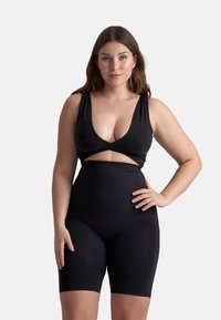 Zwarte body gemaakt van rekbaar materiaal, met een diepe V-hals, uitsnedeontwerp op de taille en een aangesloten short die tot halverwege de dij reikt.