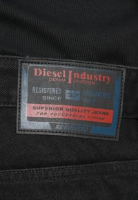 Μαύρο τζιν ύφασμα με μια εμφανή ορθογώνια ετικέτα που φέρει το λογότυπο "Diesel Industry", λεπτομέρειες εγγραφής και το κείμενο "Superior Quality Jeans".