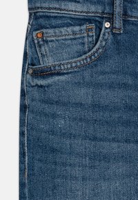 Jeans de mezclilla azul con un diseño clásico, cinco bolsillos, remaches de cobre y un ligero desgaste con una textura ligeramente usada.