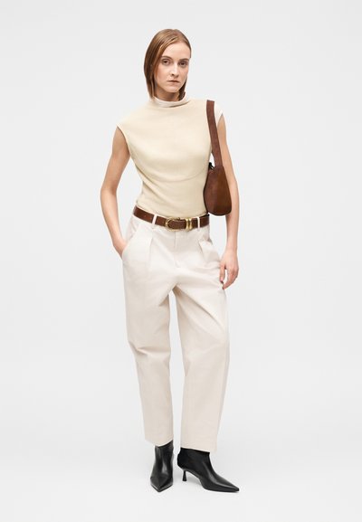 Beige ärmlös topp, krämfärgade byxor med hög midja, brunt bälte och svarta spetsiga ankelboots. Brun axelväska. Släta texturer, minimalistisk design.