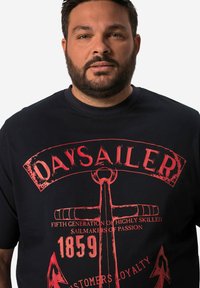 Mörkblå t-shirt med kort ärm och röd grafisk tryck med ett ankare, text och dekorativa element. Tillverkad av bomullstyg.