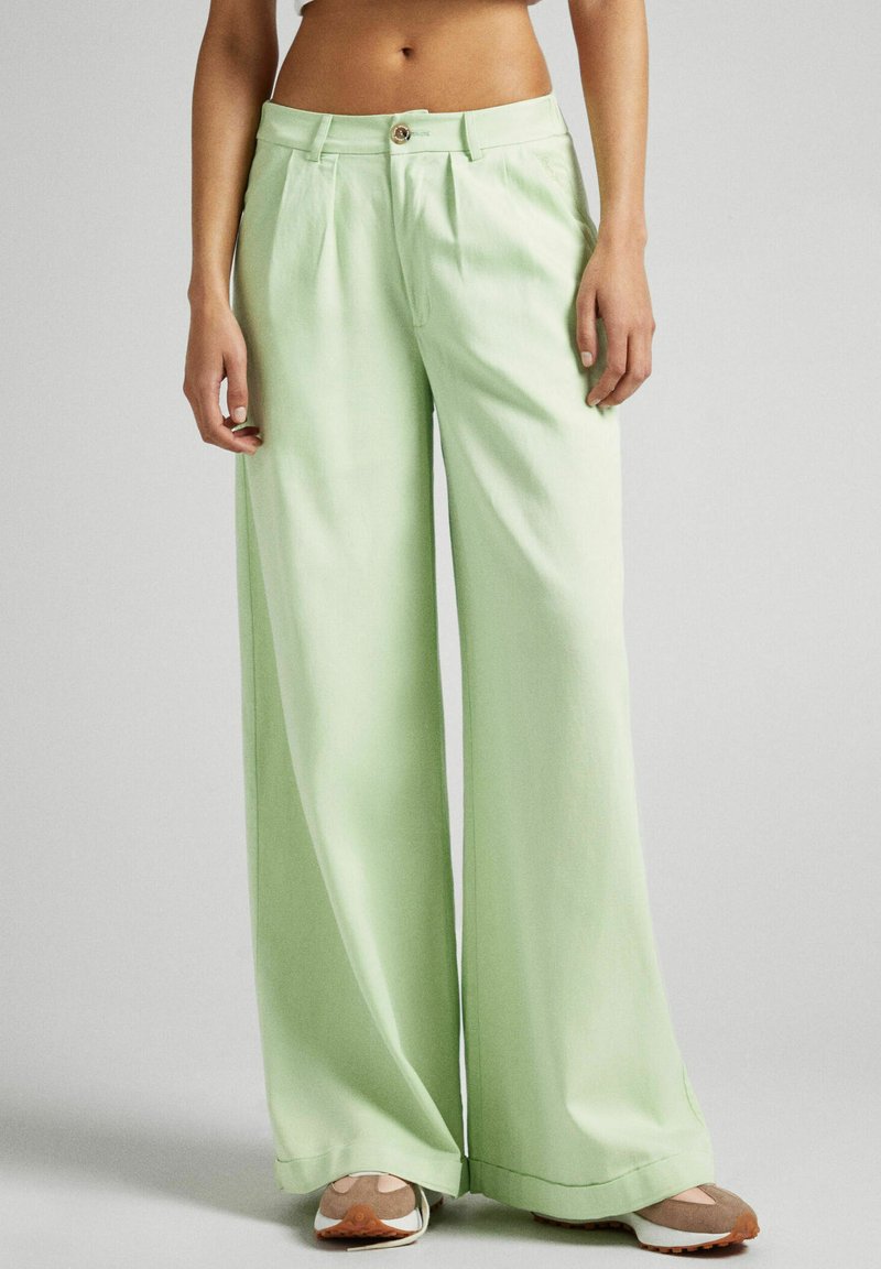 Light green wide-leg trousers with a smooth texture, front pleats, and a button closure at the waist. Paired with beige and white sneakers.