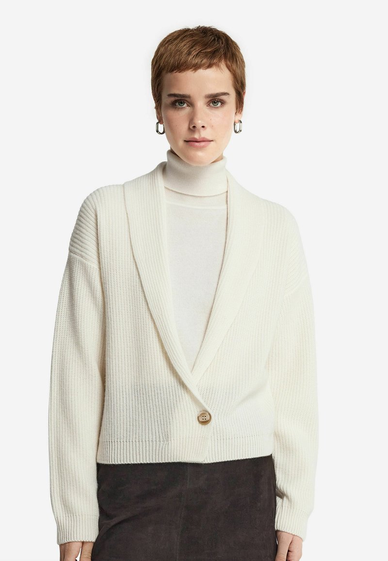Hvid ribbet cardigan med sjalkrave, der har en enkelt knaplukning og lange ærmer. Blød tekstur, cropped design.