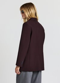 Burgundy blazer with a tailored fit, notched lapel, and long sleeves. Features four black buttons on the cuffs and a smooth fabric texture.