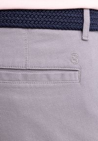 Pantalones de tela gris con acabado texturizado, que presentan una cinturilla trenzada en azul marino y un pequeño logo en el bolsillo trasero.