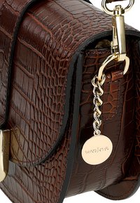 Borsa a tracolla in pelle marrone con texture a coccodrillo, accessori in oro e un'etichetta attaccata da una catena decorativa.