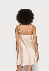 Abito slip in satin beige chiaro, dotato di spalline sottili e regolabili, con una silhouette fluida che arriva sopra il ginocchio, texture liscia.