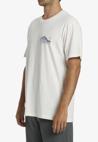 White cotton t-shirt featuring a mountain and sun graphic in blue, green, and orange. Short sleeves and a relaxed fit.