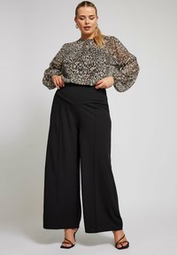 Blusa trasparente con stampa animale e maniche a sbuffo, abbinata a pantaloni neri a vita alta e gamba larga. Tacchi neri con strap completano il look.