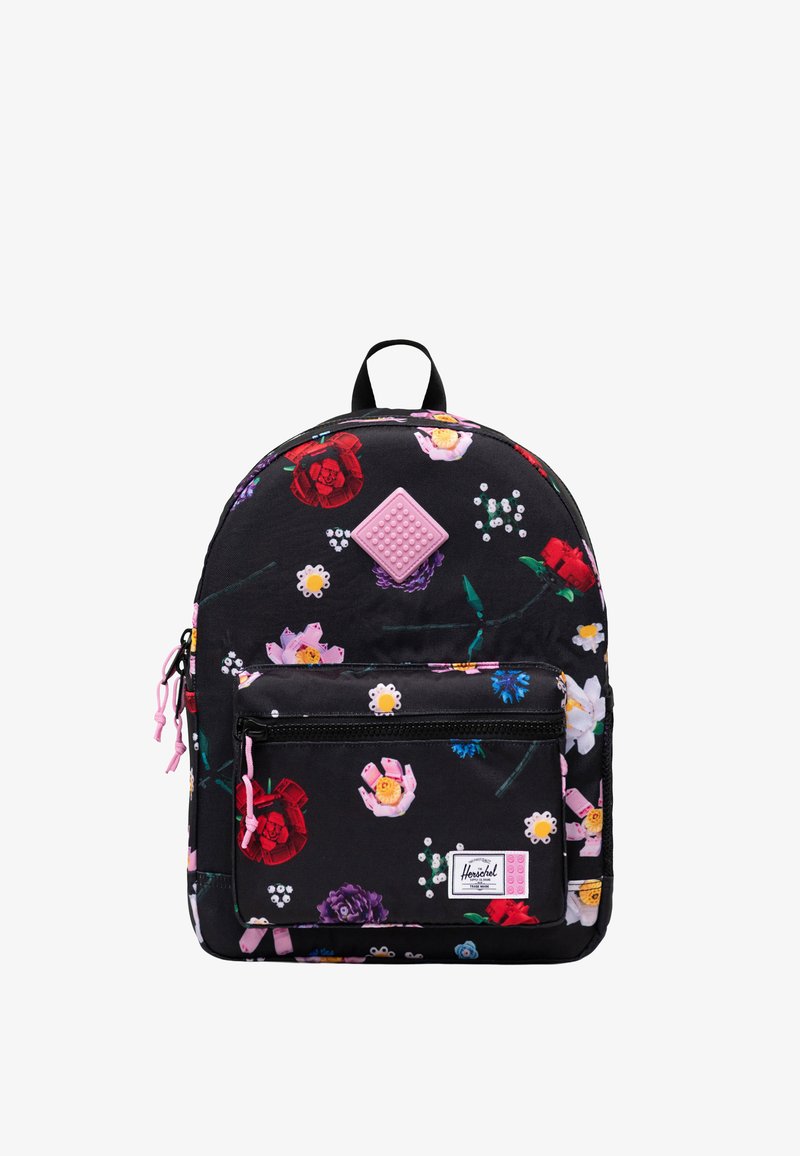 Sac à dos noir avec imprimé floral coloré, poche avant zippée, tirettes de fermeture éclair roses et petite pièce carrée rose texturée près du centre supérieur.