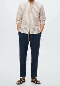 Lichtroze en witte gestreepte lange mouw shirt met een Mandarin-kraag, gecombineerd met marineblauwe broek en zwarte sandalen met banden.