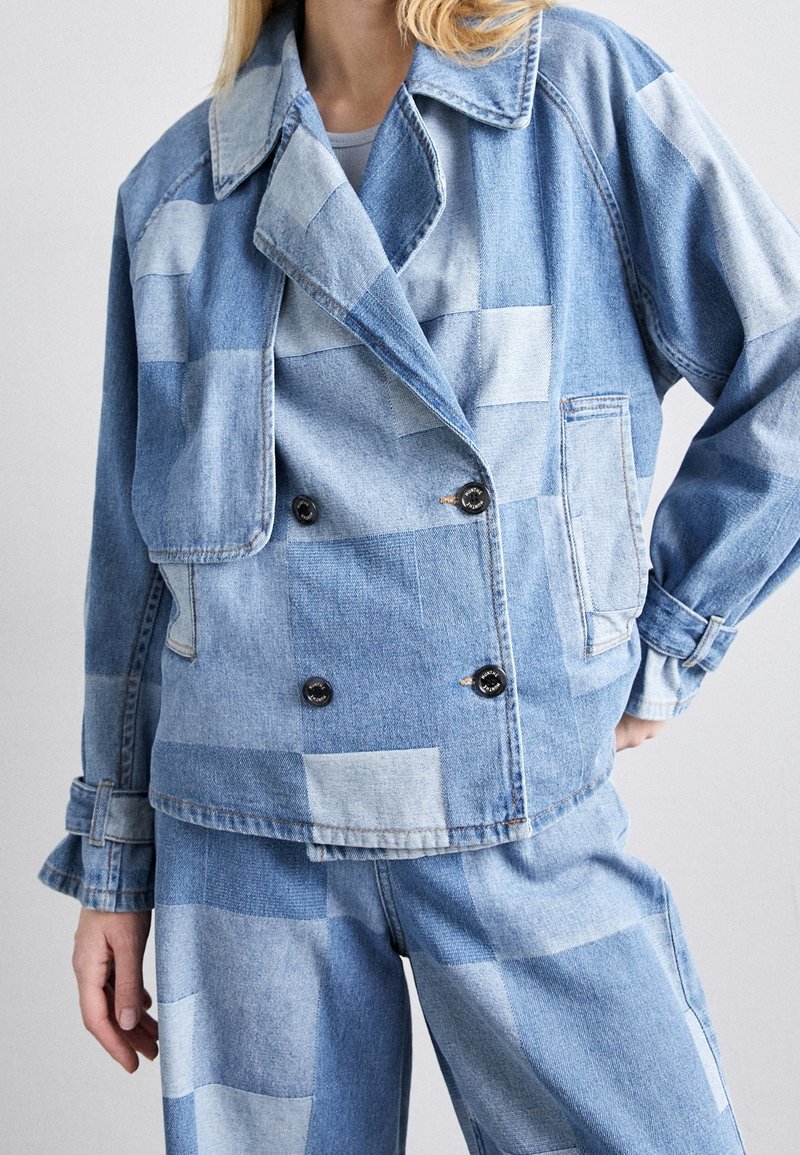 Denim jacket with a double-breasted design, featuring a patchwork pattern of light and medium blue shades, and black buttons.