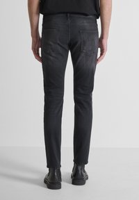 Jeans negros ajustados con un acabado desgastado, que cuentan con dos bolsillos traseros y detalles de costura. Combinados con botas negras de tobillo.