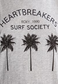 Szara bawełniana koszulka z czarnym nadrukiem przedstawiającym trzy palmy oraz napisem "HEARTBREAKERS Roxy 1990 Surf Society" powyżej.