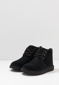 Stivaletti in suede neri con punta tondeggiante, dotati di lacci neri e suola in gomma. Accenti sottili includono occhielli in metallo e dettagli di cucitura.