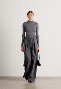 Top gris de manga larga combinado con pantalones grises de tiro alto y pernera ancha. La modelo lleva un pequeño bolso negro. Tejido suave con una sutil textura.
