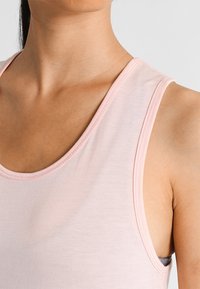 Jasnoróżowy top na ramiączkach z dekoltem w serek, cienkimi ramiączkami i gładkim, miękkim materiałem o delikatnym połysku.