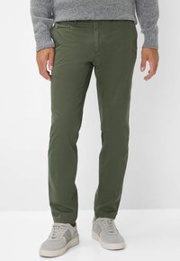 Olijfgroene slim-fit broek van katoenmix stof. Beschikt over zijzakken en een zachte textuur, gecombineerd met lichtgrijze sneakers.