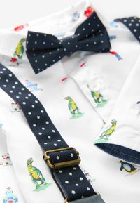 Chemise blanche avec imprimés colorés d'animaux et de robots, assortie à un nœud papillon bleu marine à pois et des bretelles avec boucle en laiton.