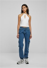 Haut halter blanc avec une découpe en trou de serrure à l'avant, associé à un jean cargo bleu moyen avec poches latérales et poignets élastiques, porté avec des baskets grises.
