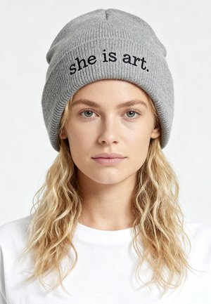 Grijze geribbelde muts met de tekst "she is art." in het zwart geborduurd. De muts heeft een nauwsluitende pasvorm en een zachte textuur.