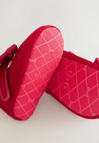 Rote Textilschuhe mit einer weichen Oberfläche, ausgestattet mit einer pinken Gummisohle und einem Rautenmuster, die mit einem Riemen für eine einfache Passform gesichert sind.